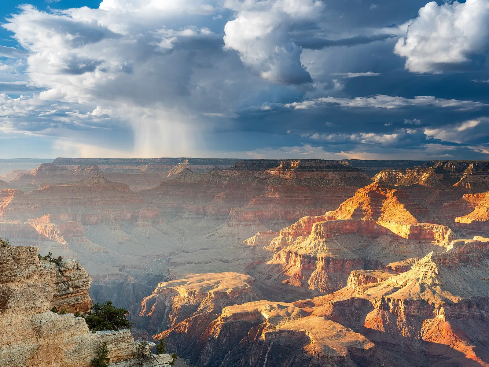 Sunlight and rain clouds over the layered cliffs of Grand Canyon National Park.