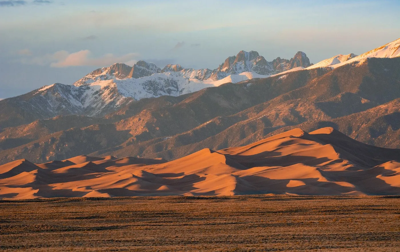 Golden sand dunes below snowy peaks in Great Sand Dunes National Park and Preserve.