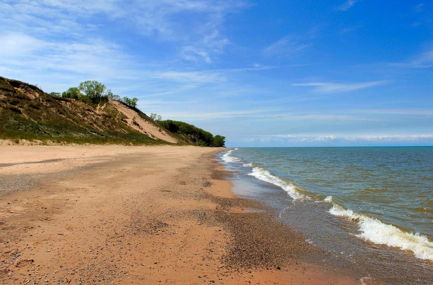 A sandy Lake Michigan beach beneath grassy dunes in Indiana Dunes National Park.