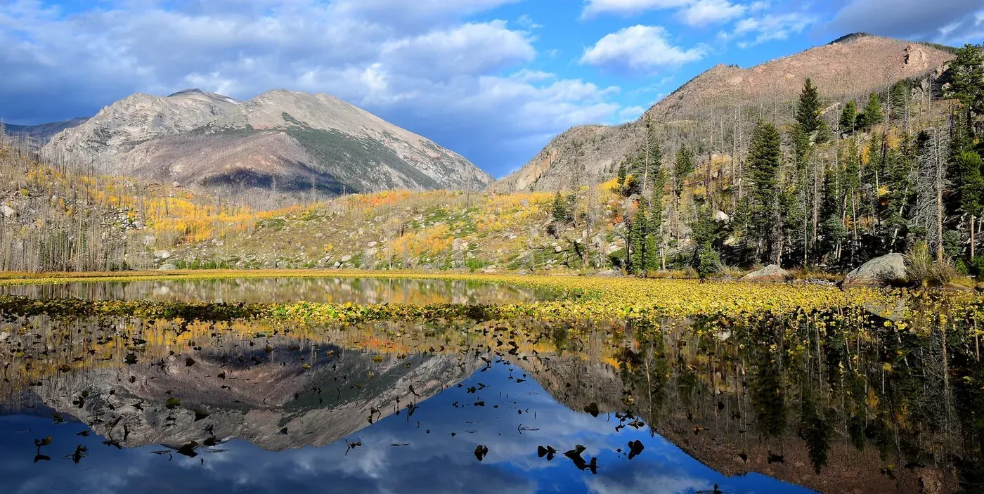 Autumn vegetation and mountain slopes reflected in Cub Lake in Rocky Mountain National Park.